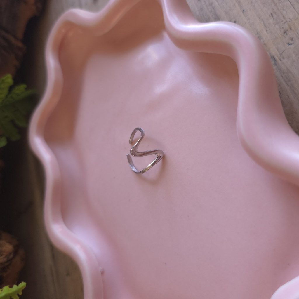 Zilverkleurige verstelbare open V-ring op een roze sieradenschaaltje