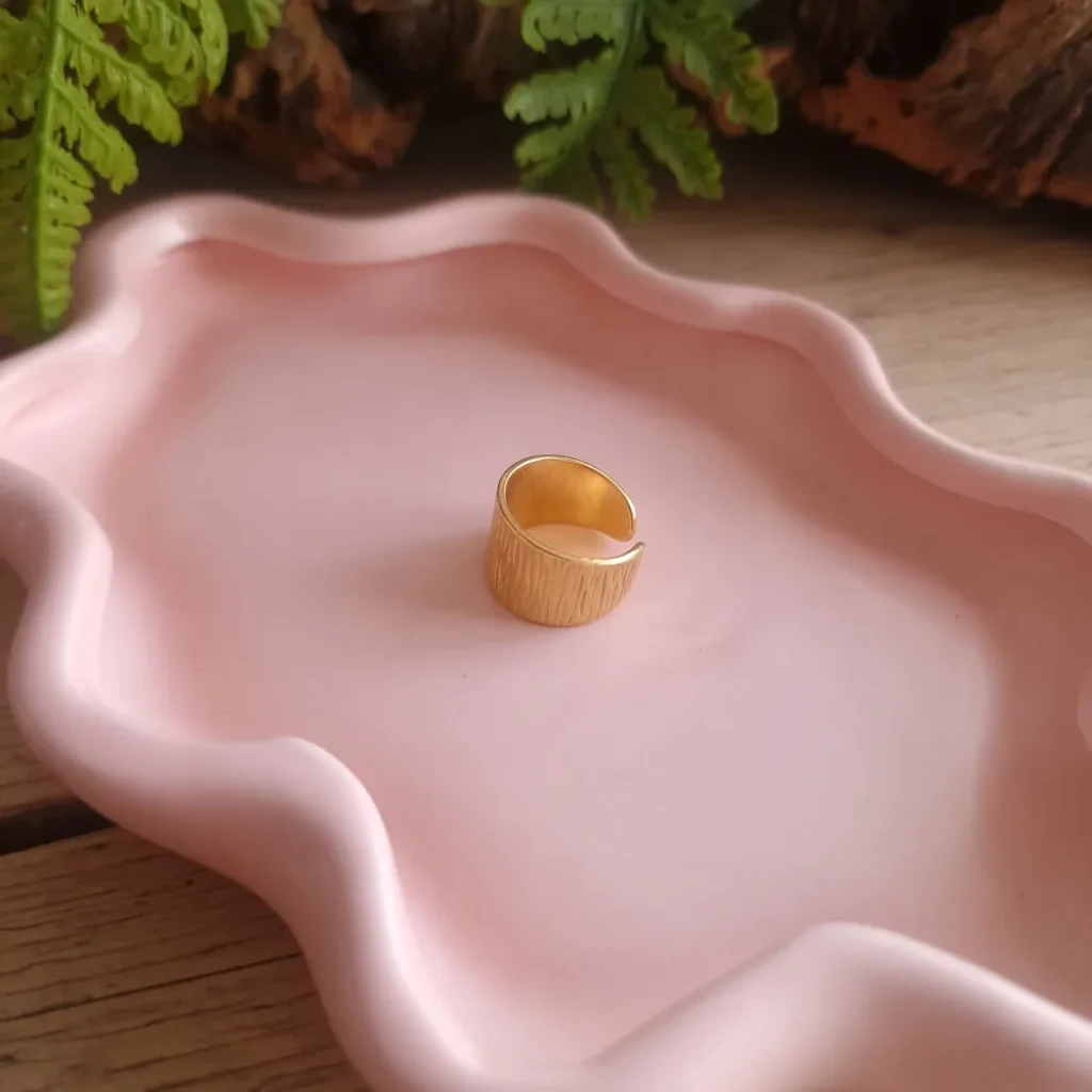 Goudkleurige brede verstelbare ring met fijne textuur op een roze sieradenschaaltje