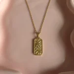 Goudkleurige ketting met rechthoekige reliëfhanger van dichtbij
