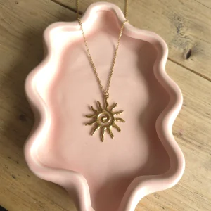 Goudkleurige ketting met zonhanger op een roze sieradenschaaltje