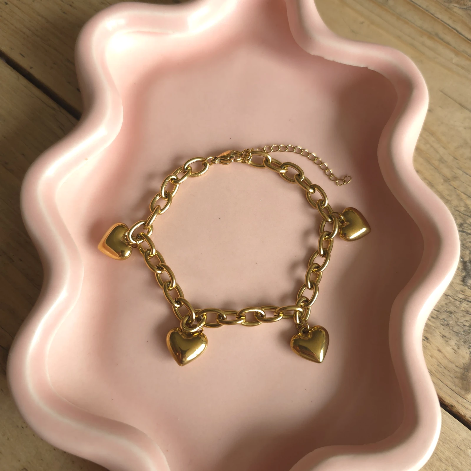 Goudkleurige schakelarmband met hartbedels op een roze sieradenschaaltje