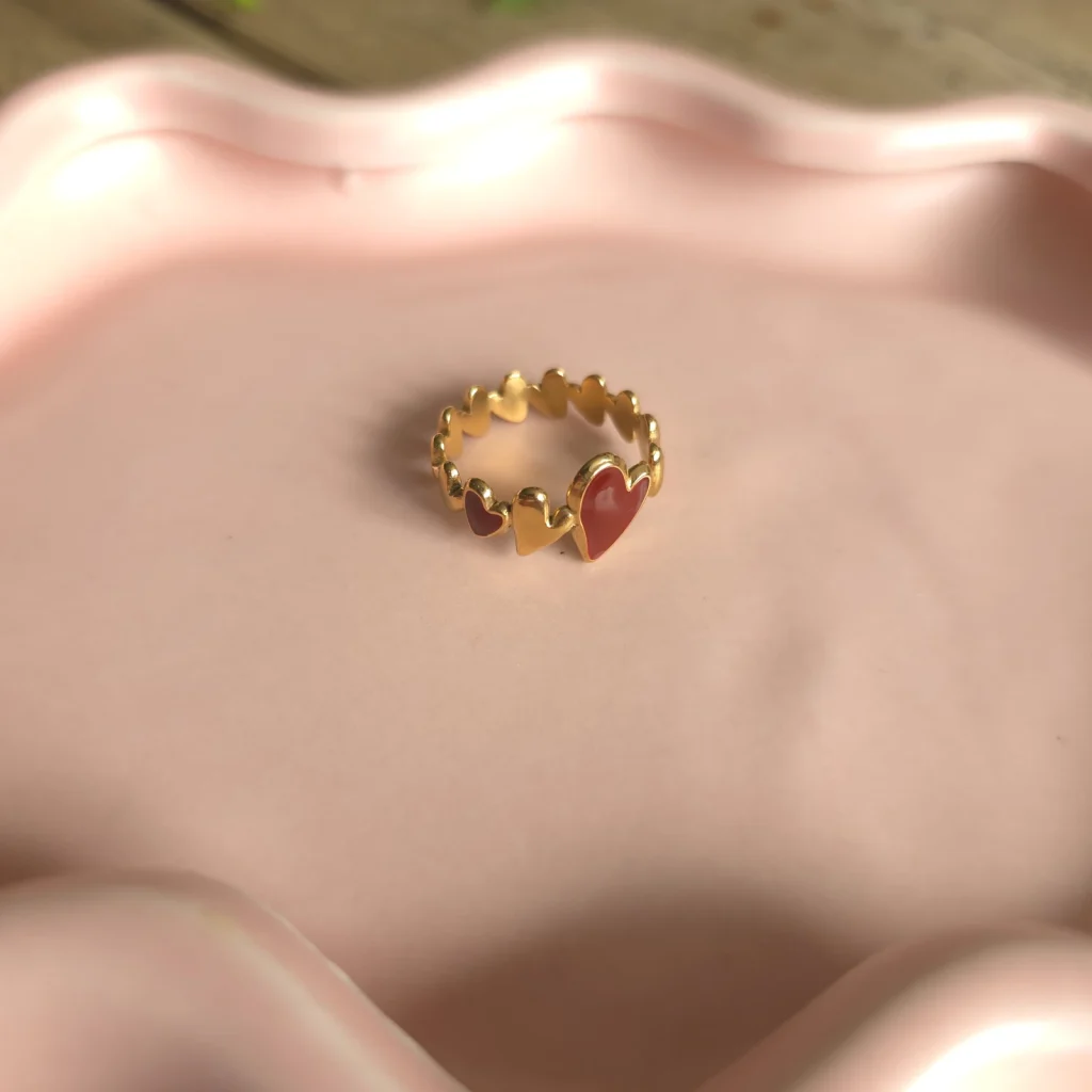 Goudkleurige verstelbare ring met rode bladdetails op een roze schaaltje