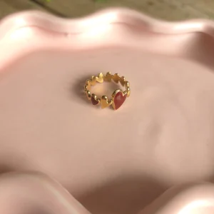 Goudkleurige verstelbare ring met rode bladdetails op een roze schaaltje